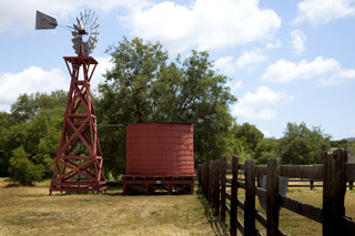 A windmill next to a fence against a blue sky with puffy clouds.