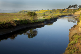A waterway cuts through a flat area with cliffs in the distance.