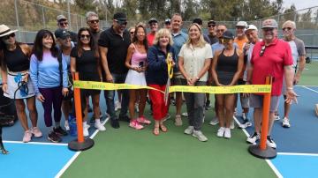 group of people cutting a ribbon at new pickleball courts.