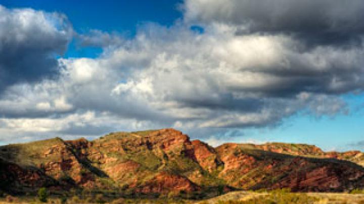 Red-hued cliffs under a blue sky with puffy clouds