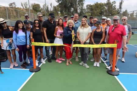 group of people cutting a ribbon at new pickleball courts.